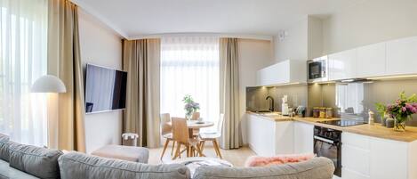 A modern living room with a grey sofa, a dining area with a table and chairs, and a kitchen with white cabinets and a microwave.