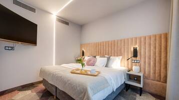A hotel room with a bed, a bedside table, a TV mounted on the wall, and a wall-mounted air vent.