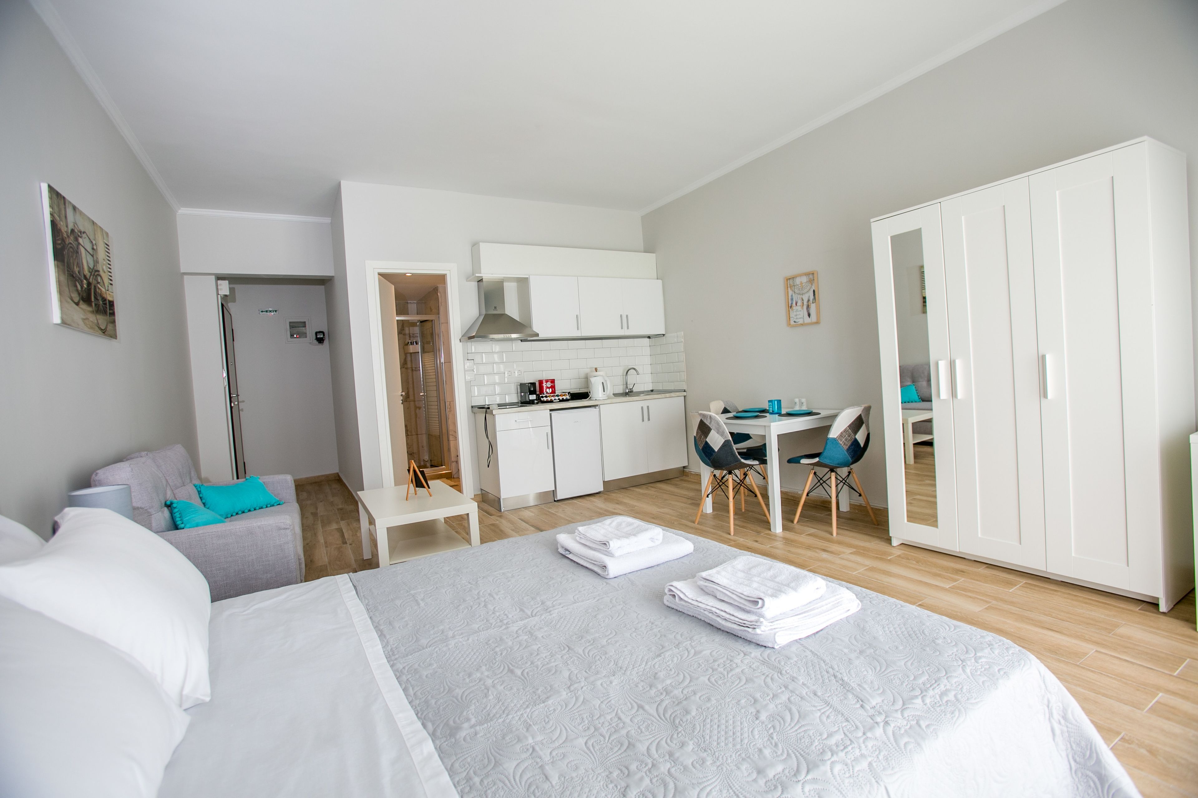 A compact hotel room with a bed, a desk, kitchenette, and a wardrobe.