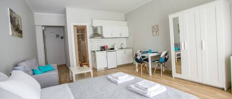 A compact hotel room with a bed, a desk, kitchenette, and a wardrobe.