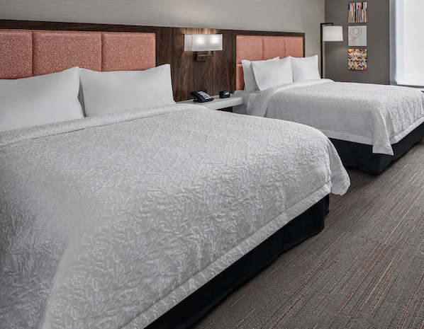 A hotel room with two beds, a wooden headboard, a bedside table with a phone, and artwork on the wall.