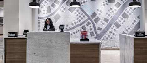 A hotel reception desk with a modern design, a check-in counter, and a digital kiosk.