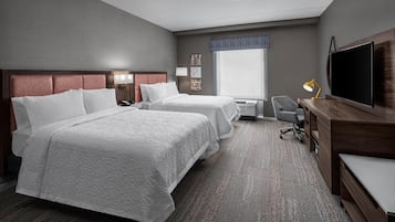 A hotel room with two beds, a desk, a TV, and a window.