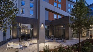 A modern building with large windows, outdoor seating, and a well-maintained garden.