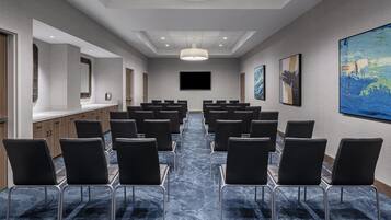 Un salón de conferencias con filas de sillas, una pantalla grande y obras de arte en las paredes.