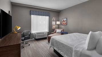 A hotel room with a bed, desk, chair, air conditioning unit, and a TV.