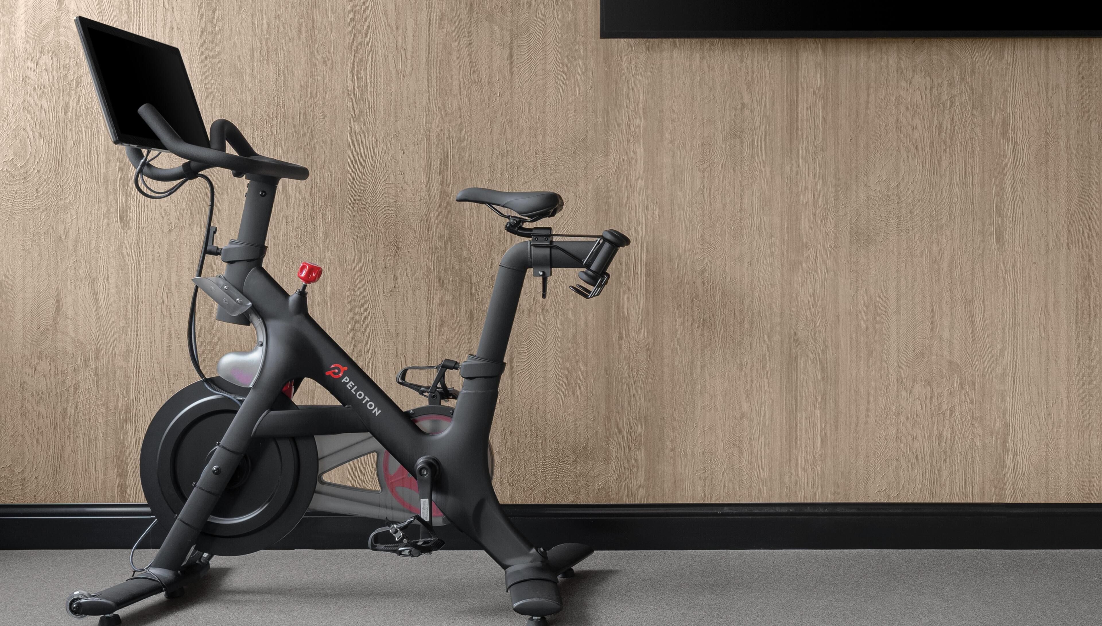 Ein stehendes Ergometer mit digitalem Display, vor einer Holzwand platziert.