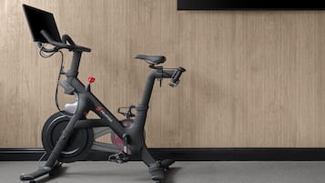 Ein stehendes Ergometer mit digitalem Display, vor einer Holzwand platziert.