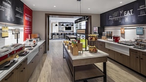 A modern kitchen with a central island, bar seating, and a variety of food items displayed.