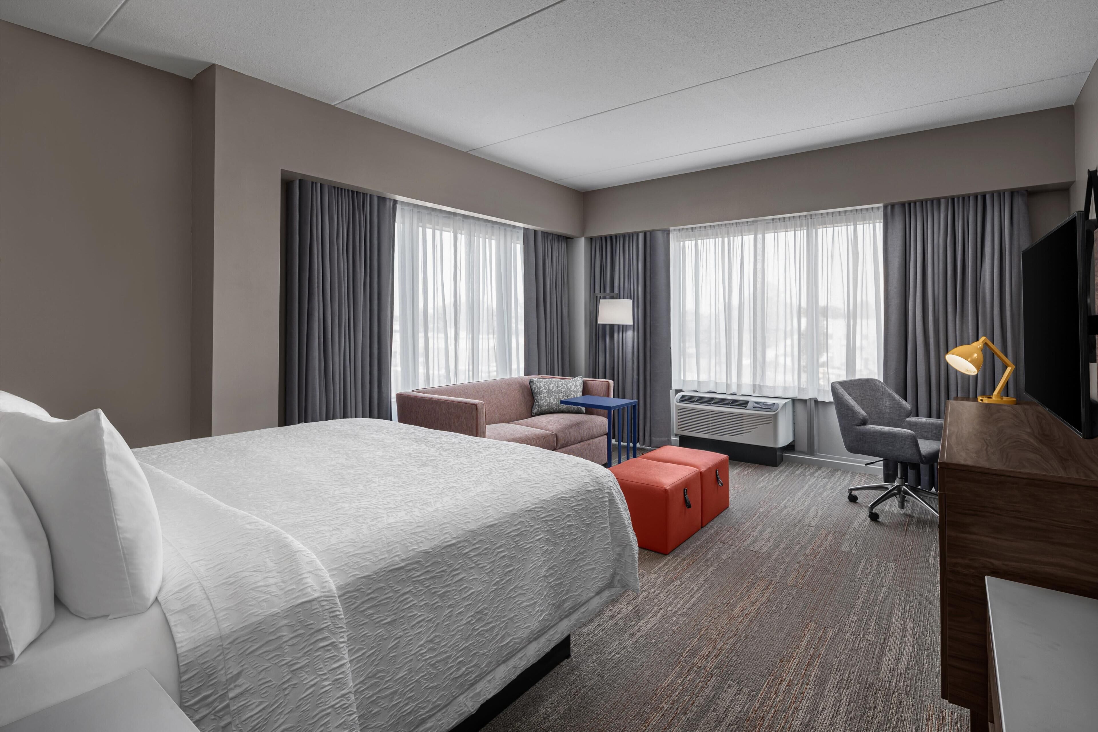 A hotel room with a large bed, a desk, a chair, a sofa, and a TV.