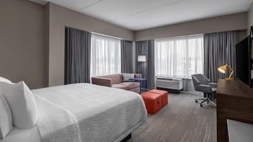 A hotel room with a large bed, a desk, a chair, a sofa, and a TV.