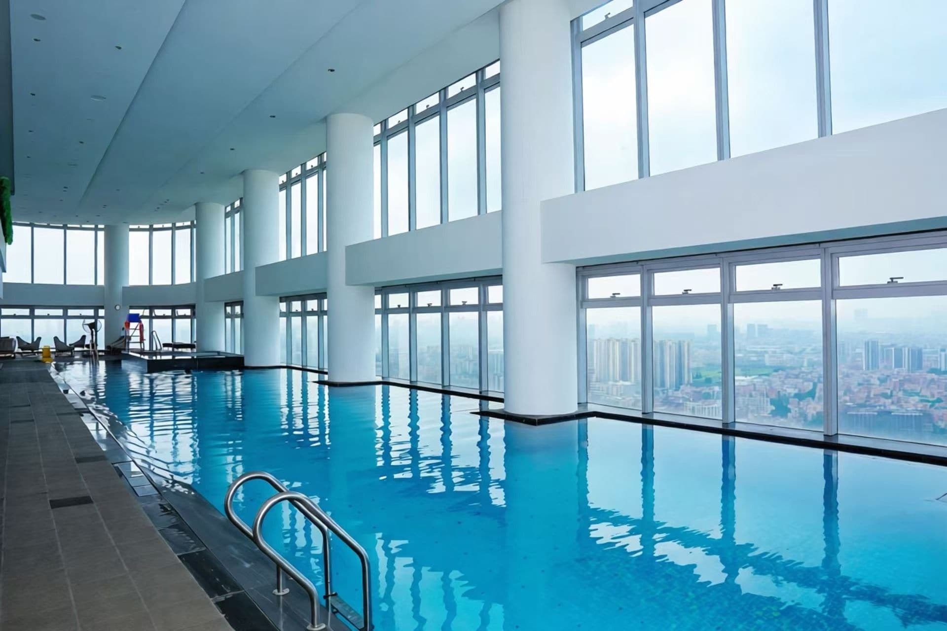 Una piscina interior con vistas despejadas de un paisaje urbano a través de amplios ventanales.