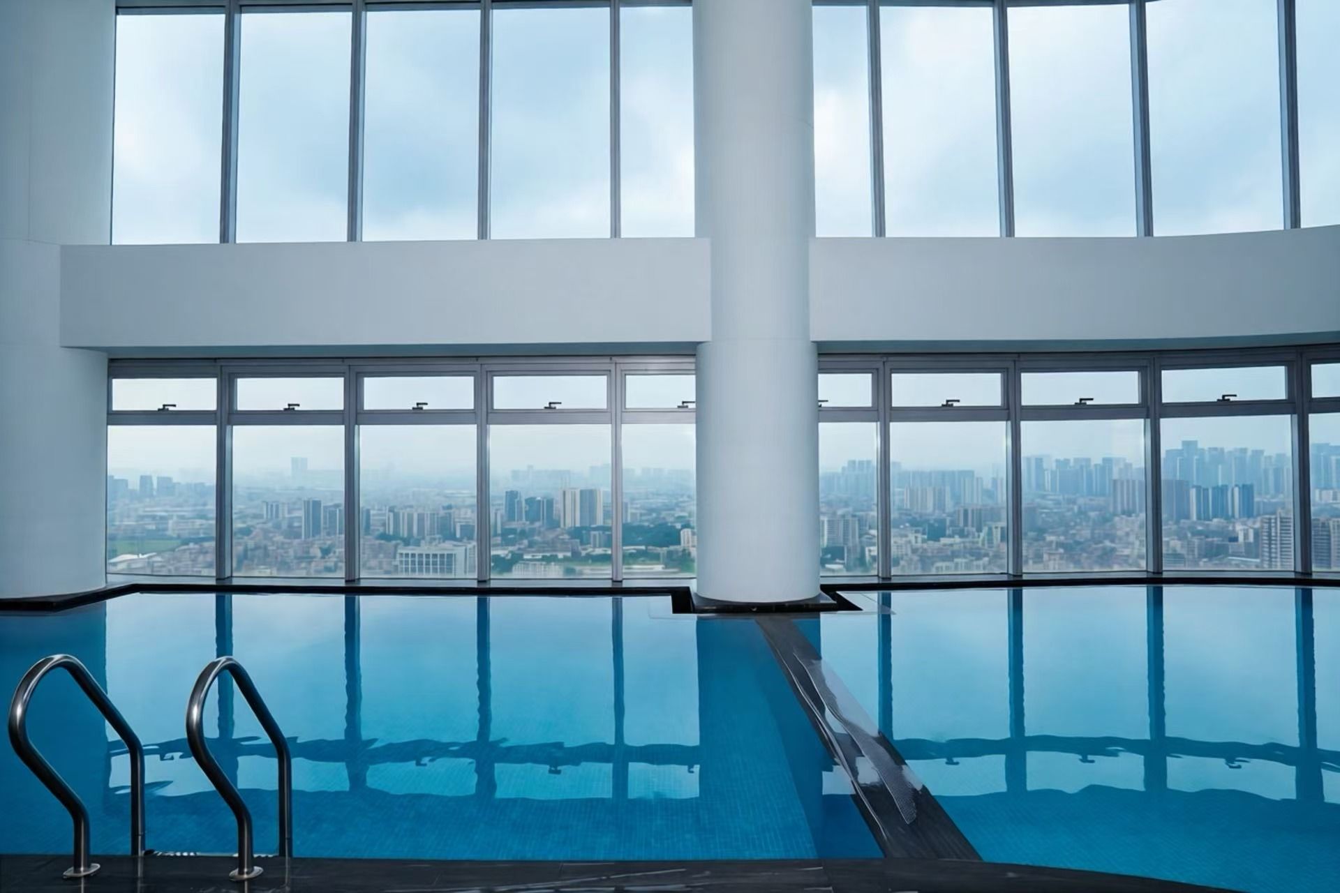 Une piscine à débordement intérieure offrant une vue sur la ville grâce à de grandes fenêtres.