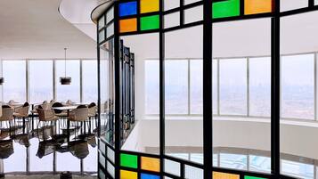 A modern interior with large windows, a glass partition with colorful panels, and a dining area with wicker chairs.