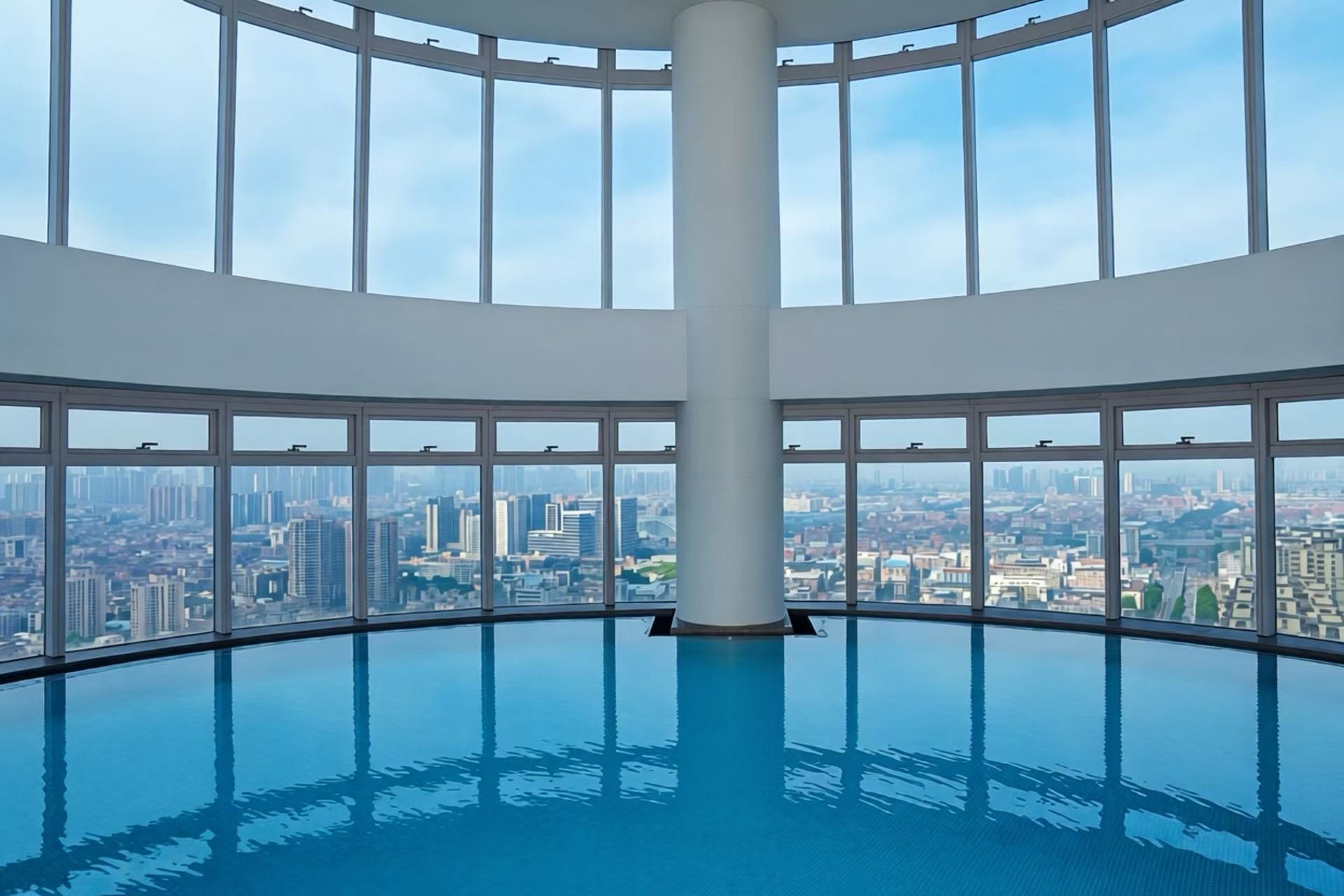 A large indoor swimming pool with a cityscape view through the surrounding windows.