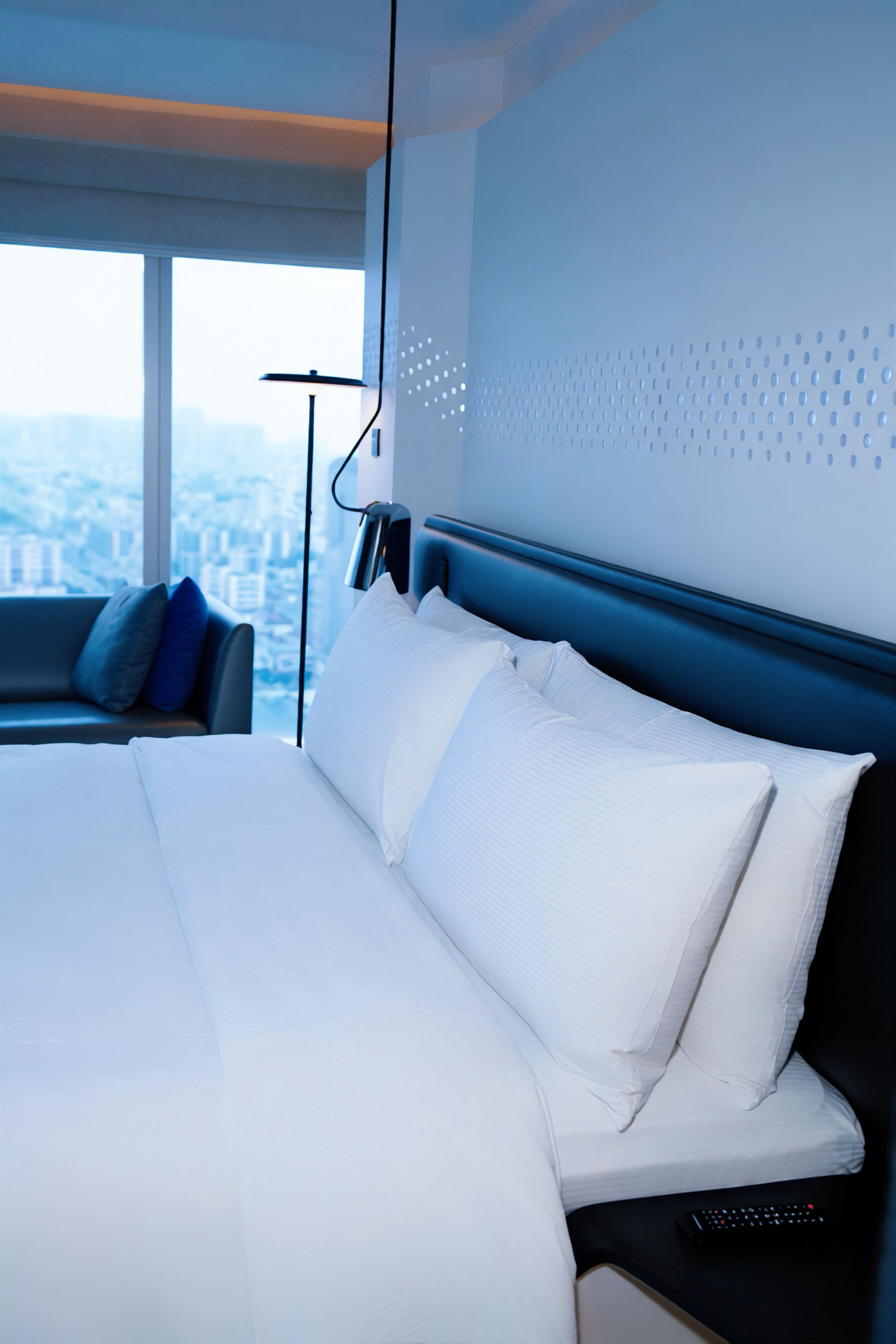 A modern hotel room with a large bed, a view of the city, and a cityscape visible through the window.
