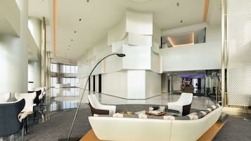 A spacious lobby with a modern design, featuring a central seating area with a sofa and armchairs, a coffee table, and a floor lamp.