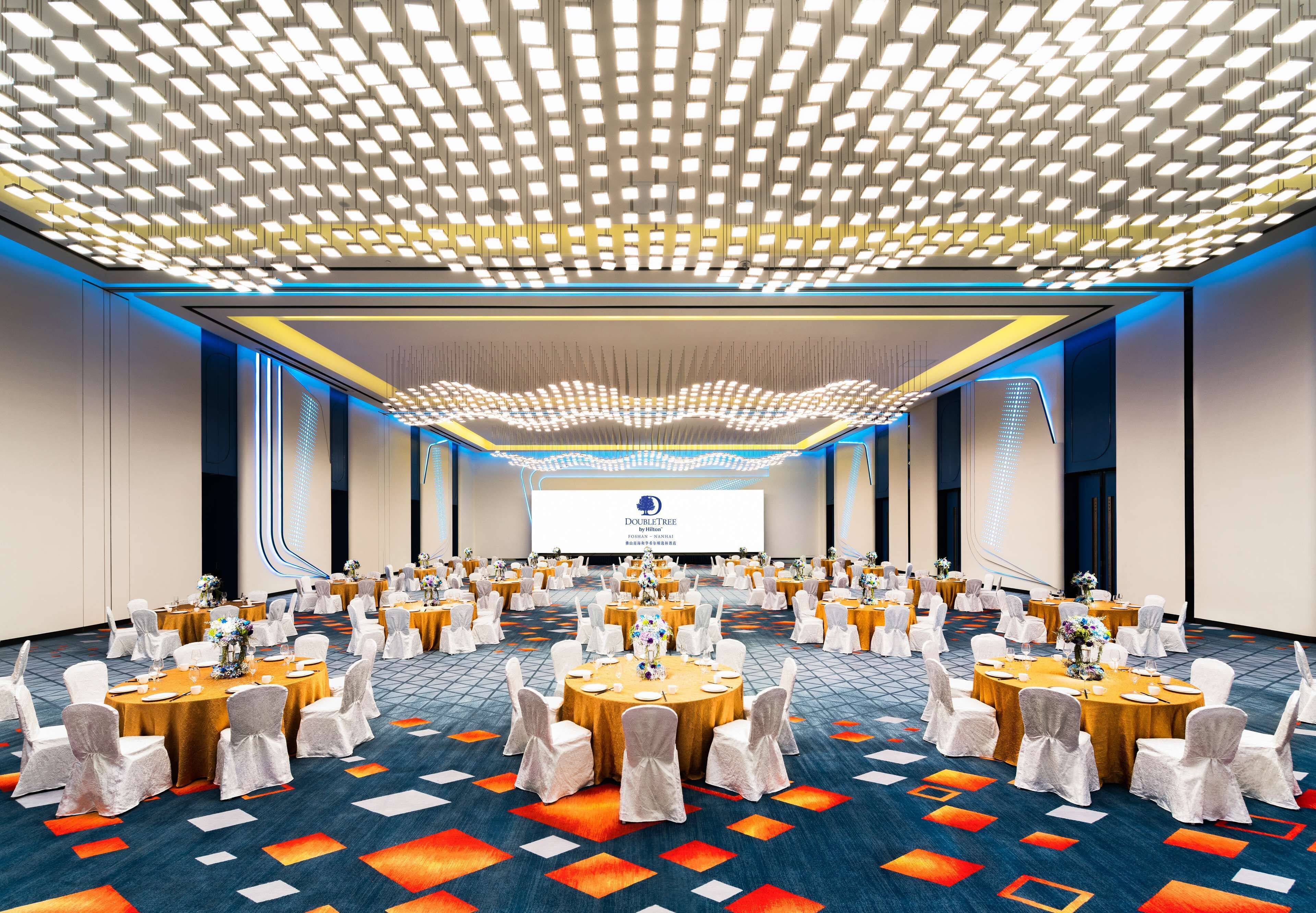 A conference room with round tables, white chairs, and a large screen at the front.