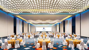 A conference room with round tables, white chairs, and a large screen at the front.