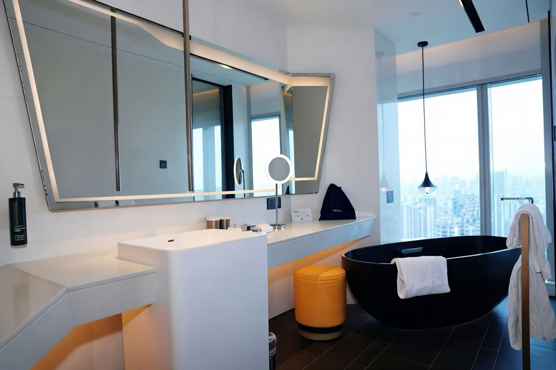 A modern bathroom with a large mirror, a black bathtub, and a city view.