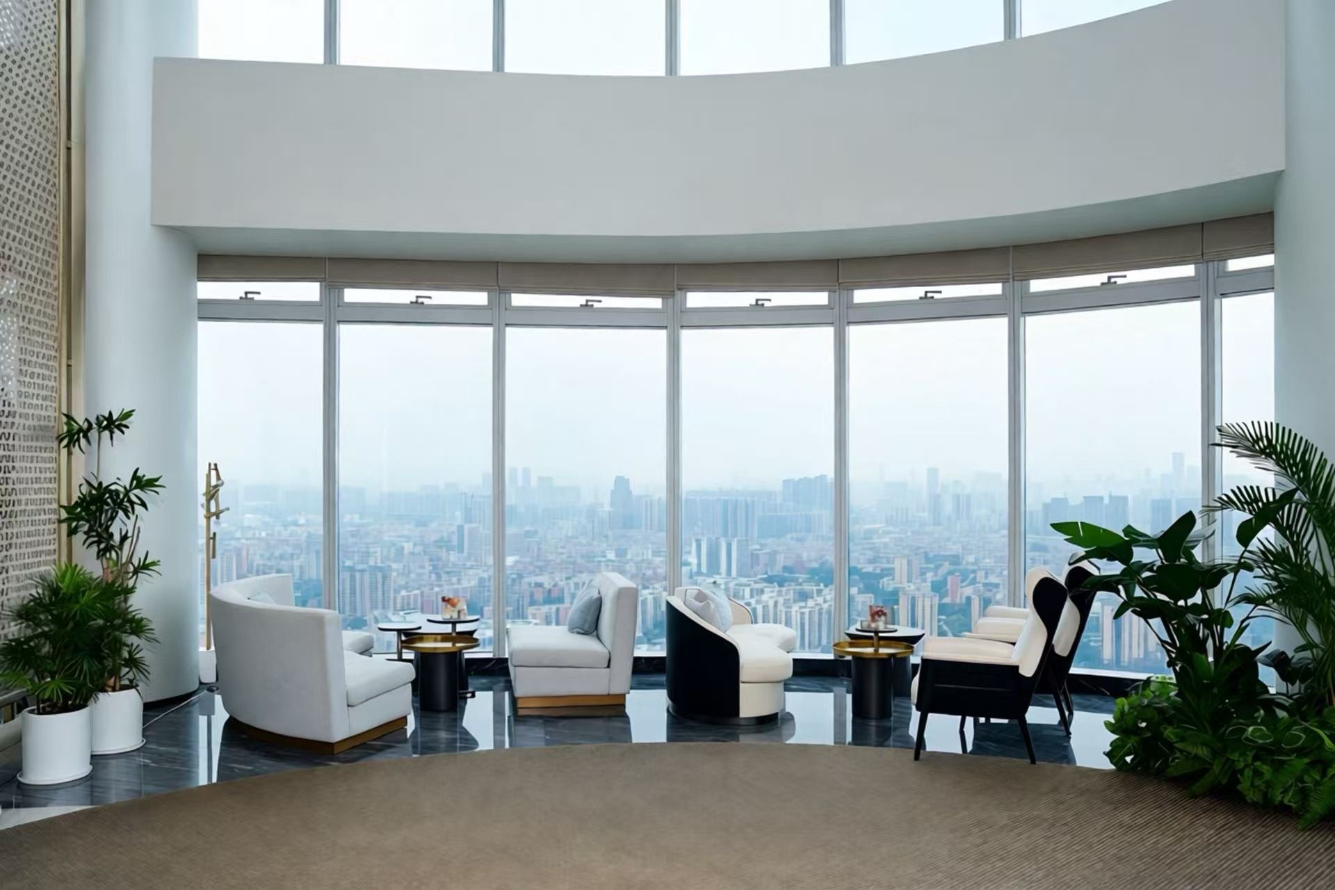 A high-rise interior with a panoramic city view, modern furniture, and indoor plants.