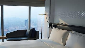 A modern hotel room with a large bed, a sofa, a city view, and a unique wall design.