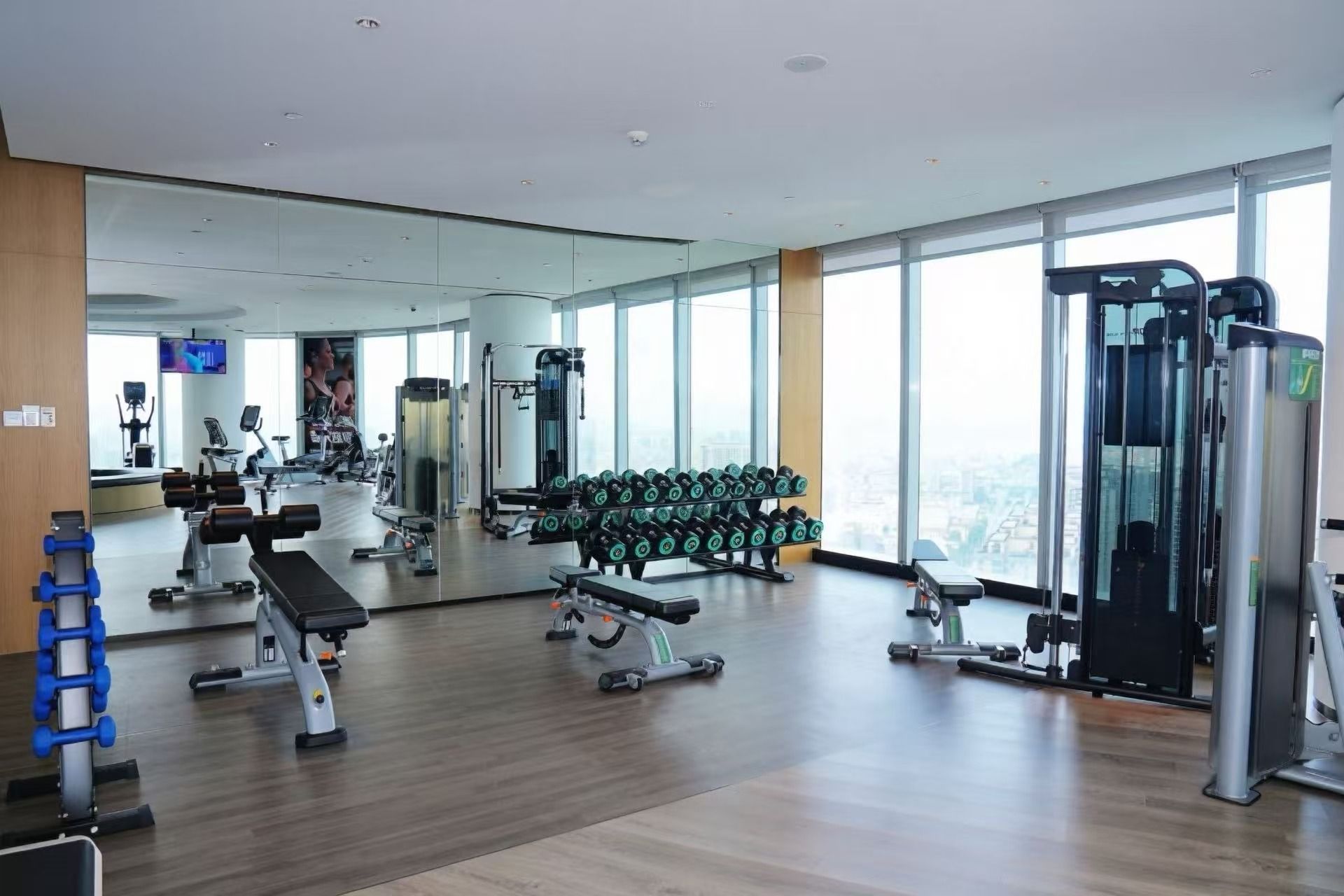 Un gimnasio con equipo de ejercicio diverso, un espejo grande y amplias ventanas.