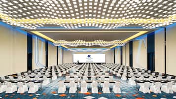 A conference room with rows of tables and chairs, a large screen at the front, and a patterned ceiling.