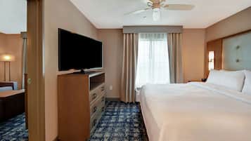 A hotel room with a bed, a television on a wooden dresser, a ceiling fan, and a window with curtains.