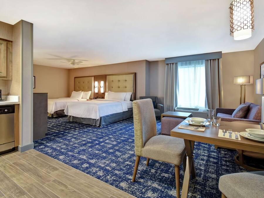 Quarto de hotel com duas camas, área de refeições, cozinha e sala de estar.