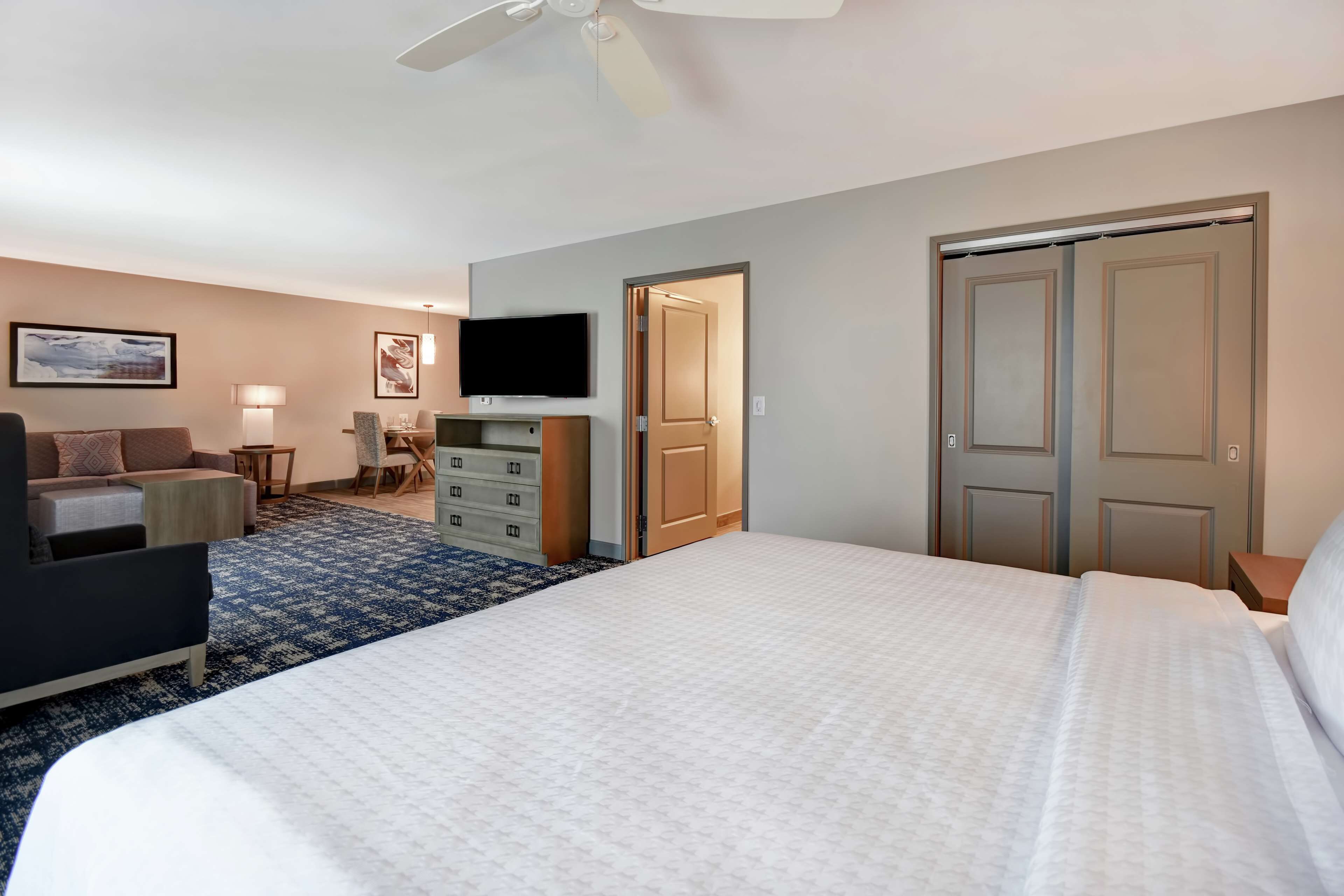 A hotel room with a large bed, a desk, a chair, a television, and a wardrobe.