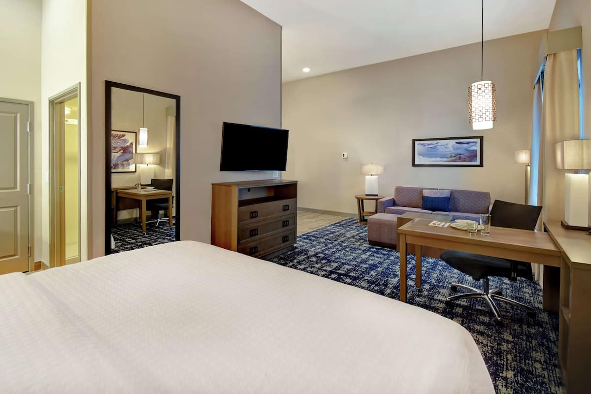 A hotel room with a large bed, a desk with a chair, a sofa, a TV, and a desk lamp.
