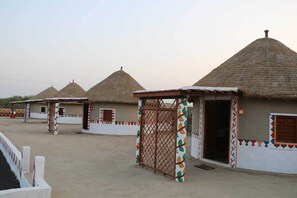 A row of traditional thatched-roof huts with decorative patterns and a gated entrance.