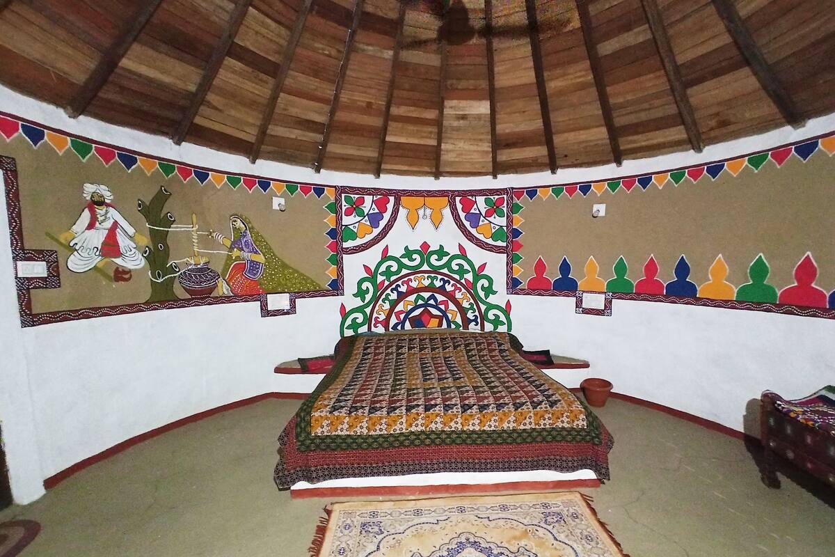 A room with a bed, a colorful wall mural, and a patterned rug.