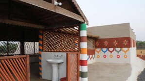 A building with a thatched roof, a white sink, and a colorful wall with geometric patterns. - Banni Village Stay (Bhuj)