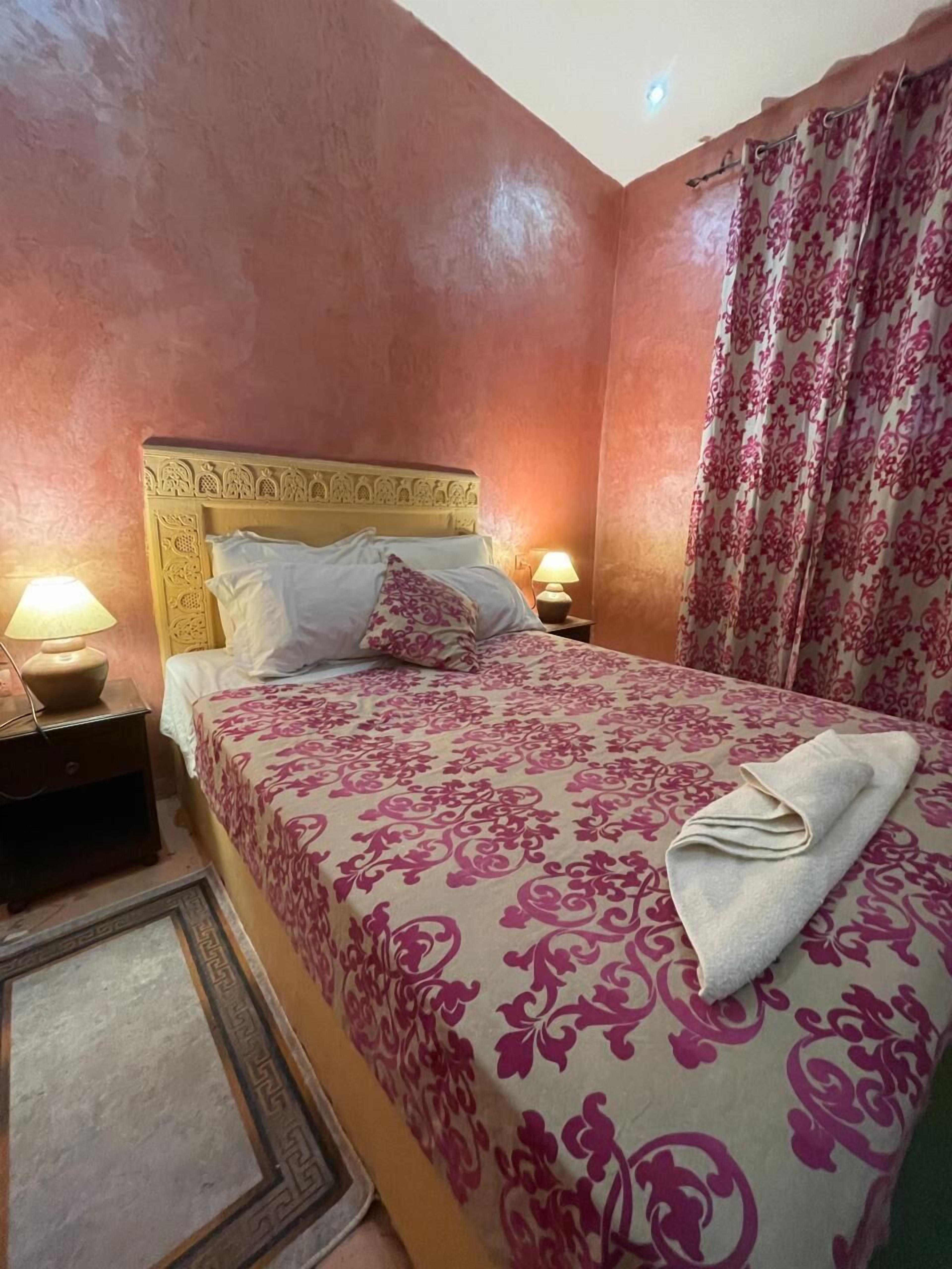 A bedroom with a bed, two bedside lamps, a patterned bedspread, and a curtain.