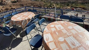 Terraço ao ar livre com mesas e cadeiras, com vista para uma paisagem montanhosa e uma aldeia distante.