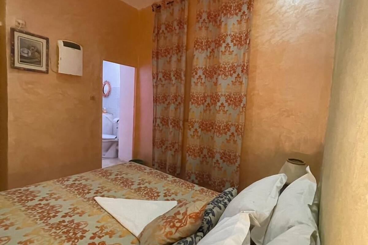 A bedroom with a bed, a bedside table, and a mirror. There is a door leading to a bathroom.