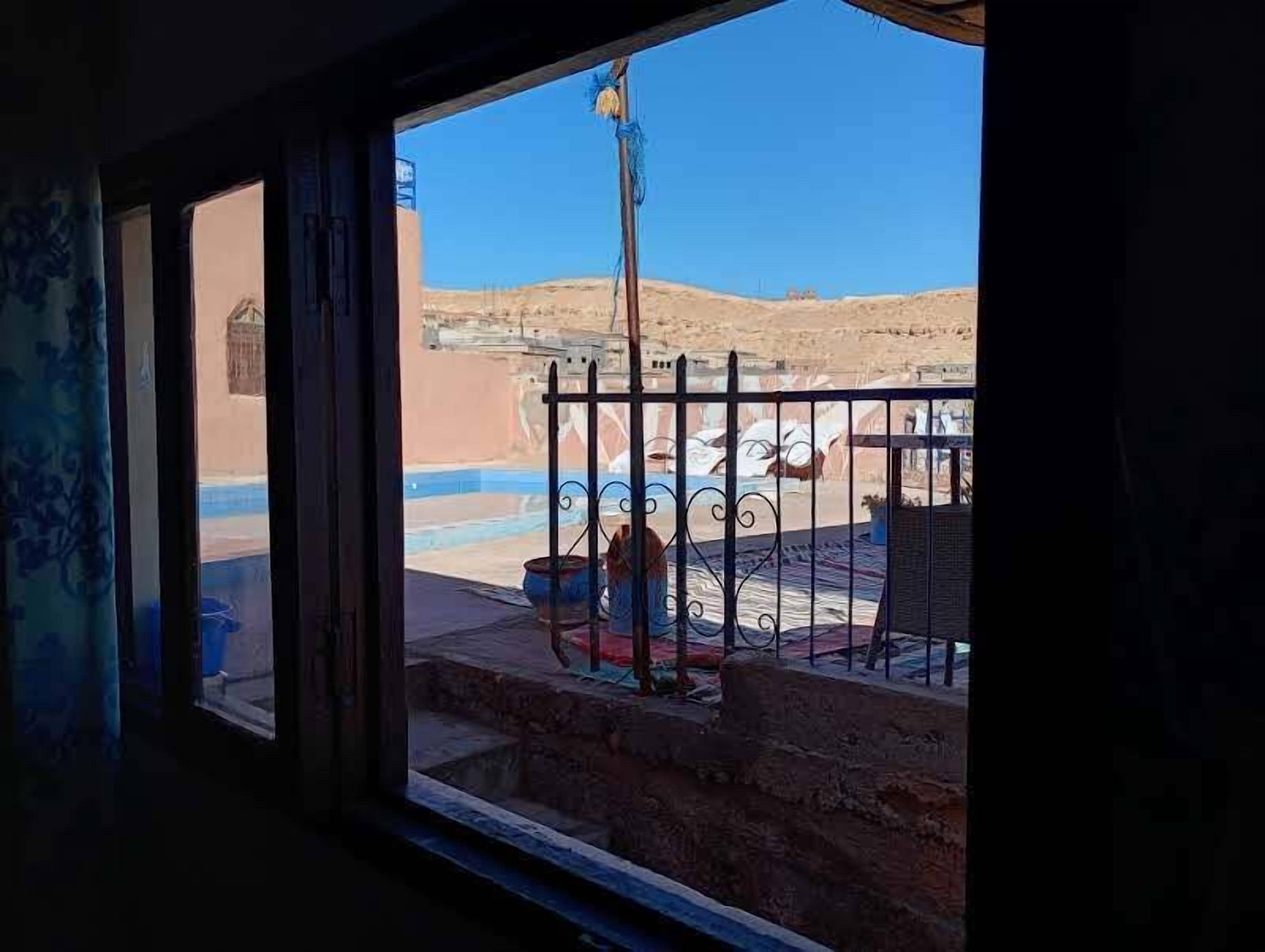 A view from a window with a metal railing, a pool, and a desert landscape.