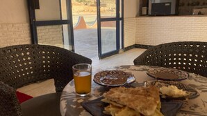 Uma área de refeições com uma mesa posta para dois, incluindo um copo de cerveja, um prato de comida e um pão achatado.