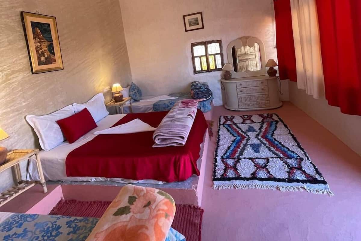 A hotel room with two beds, a large rug, a dresser, and a window with red curtains.