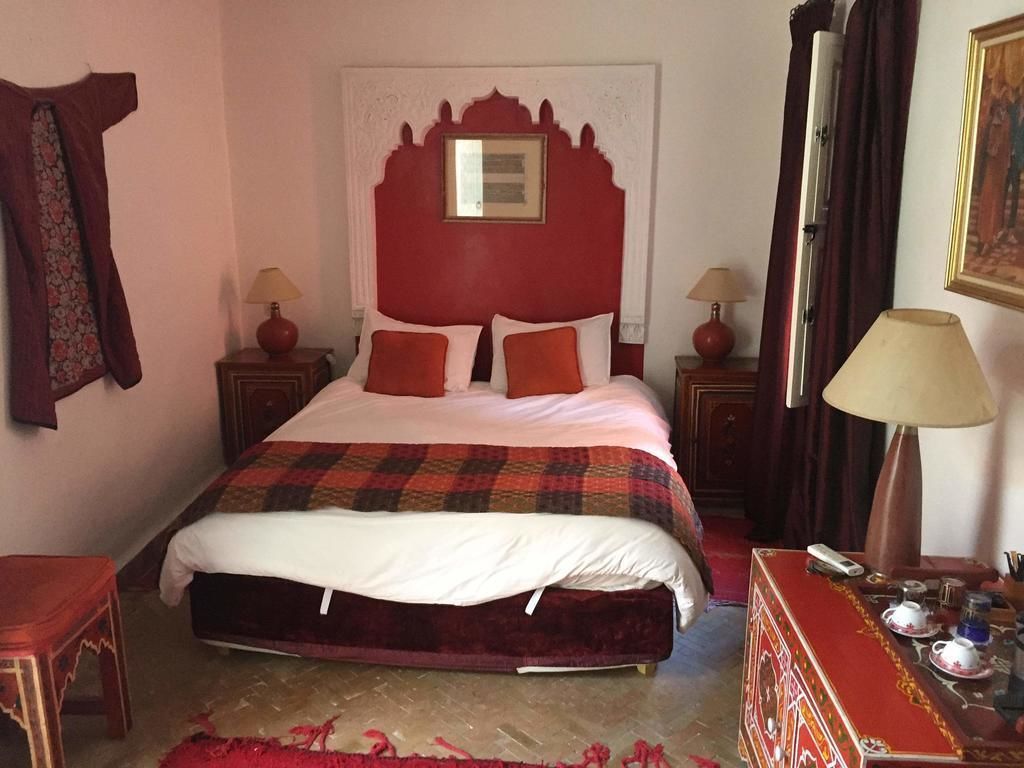 A hotel room with a large bed, two bedside tables, a red headboard, and a red carpet.
