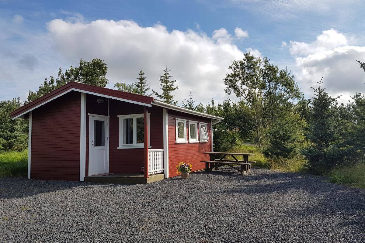 A small, single-story cabin with a red exterior and white trim, a front door, and a small porch area.