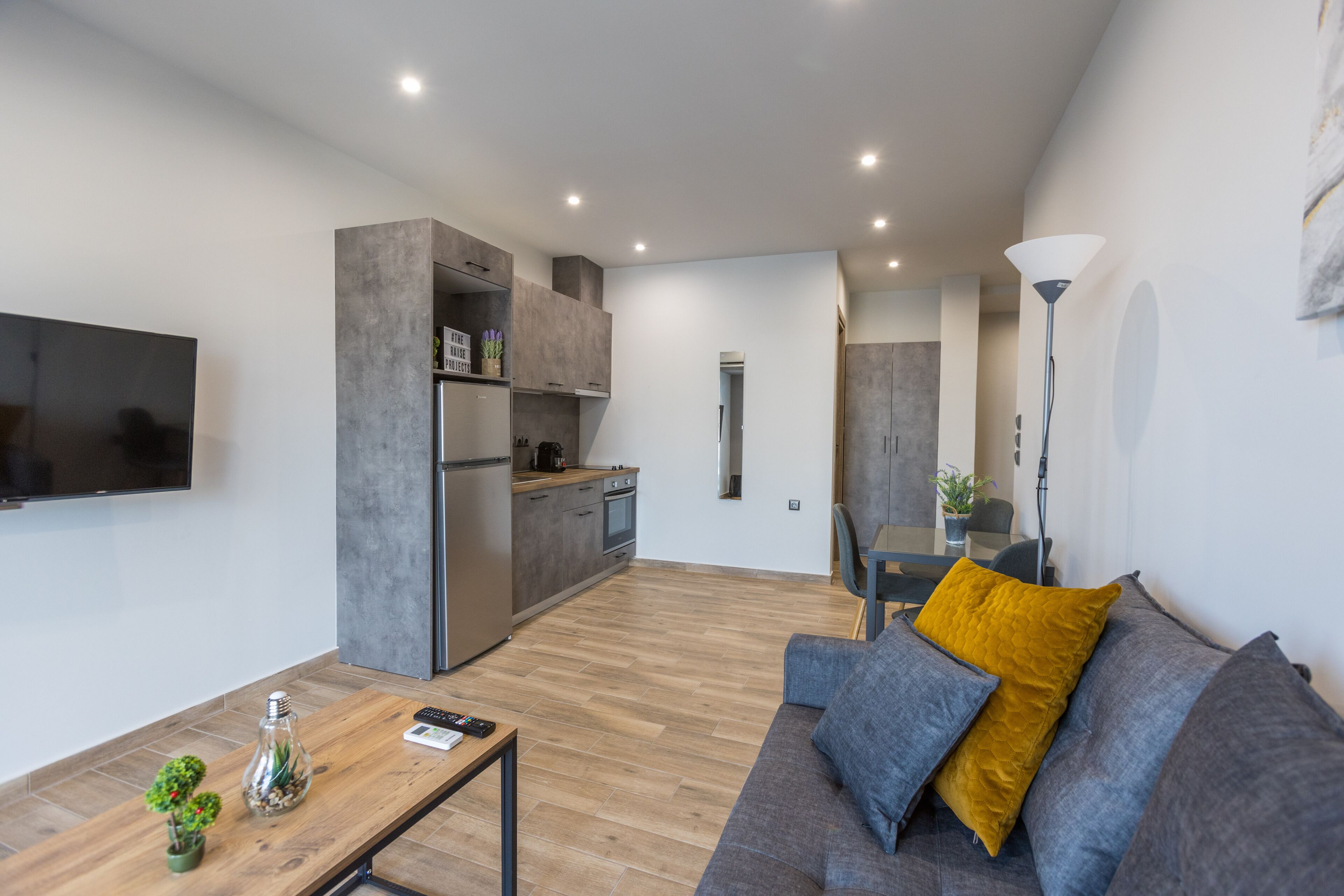 Un espace de vie moderne comprenant une cuisine, un coin repas et un canapé agrémenté d’un coussin de couleur moutarde.