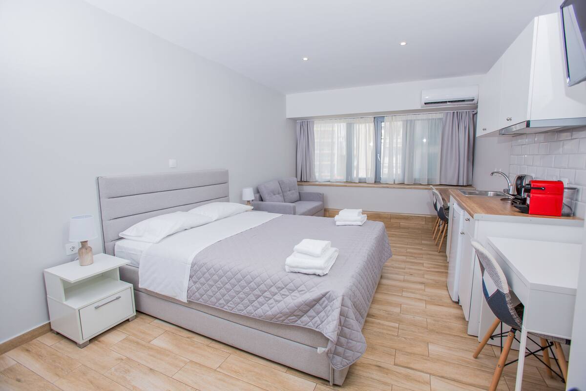 Habitación de hotel moderna con cama, mesita de noche, lámpara y vista al área de la cocina.