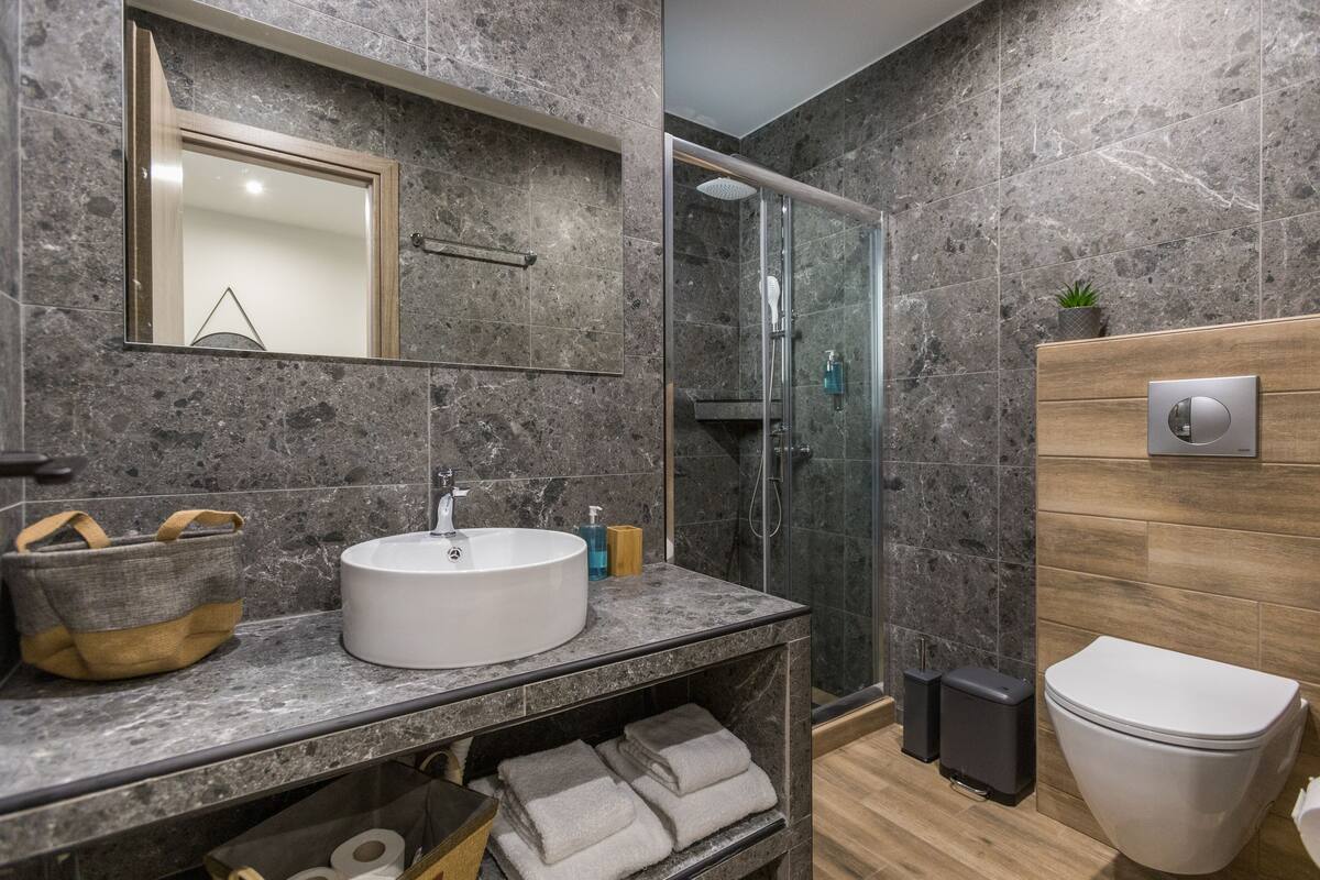 Un baño moderno con lavamanos de mármol, cabina de ducha con paredes de cristal, tocador de madera y un inodoro.