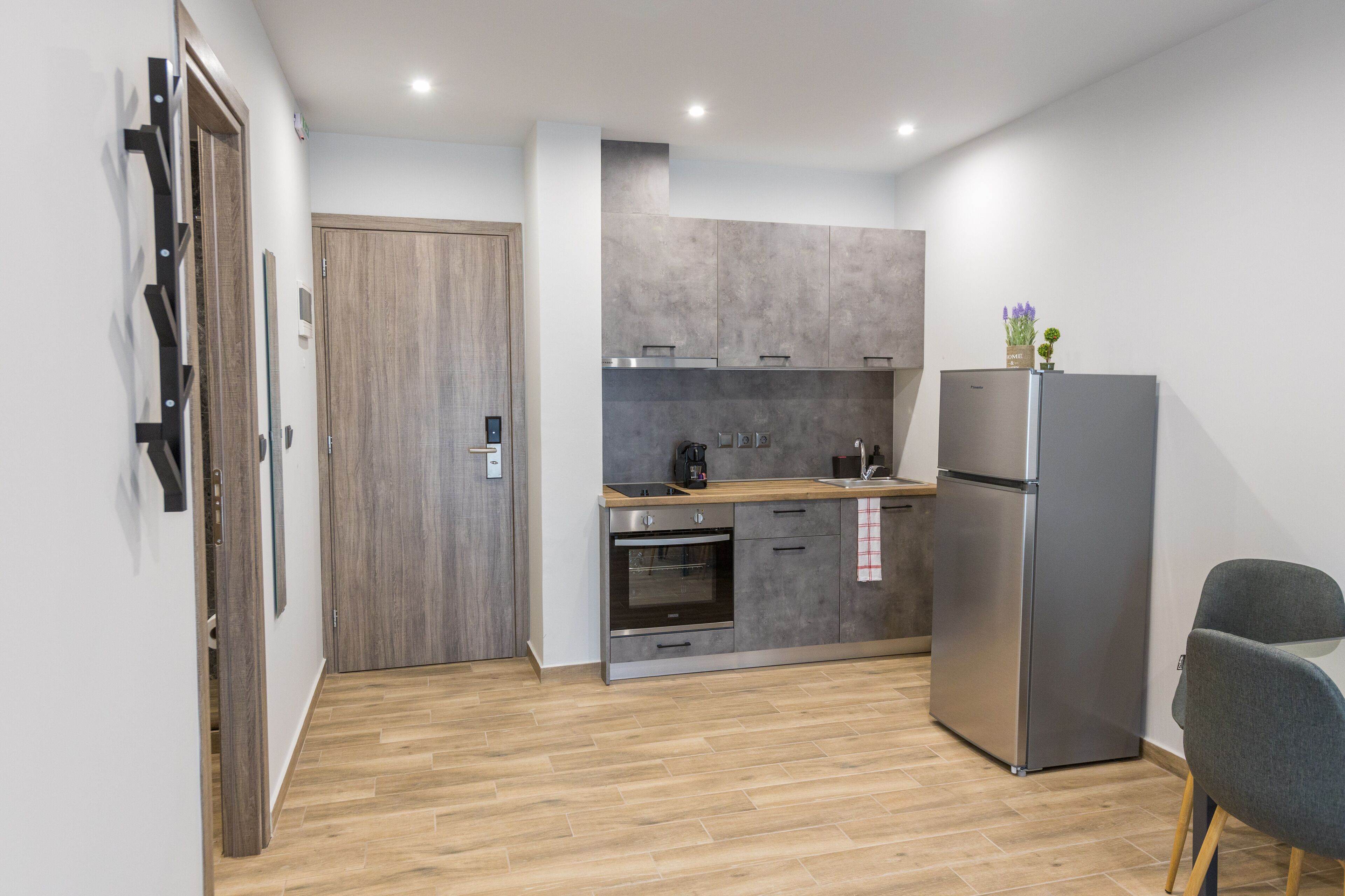 A modern kitchen with grey cabinets, a stainless steel refrigerator, and a wooden countertop.