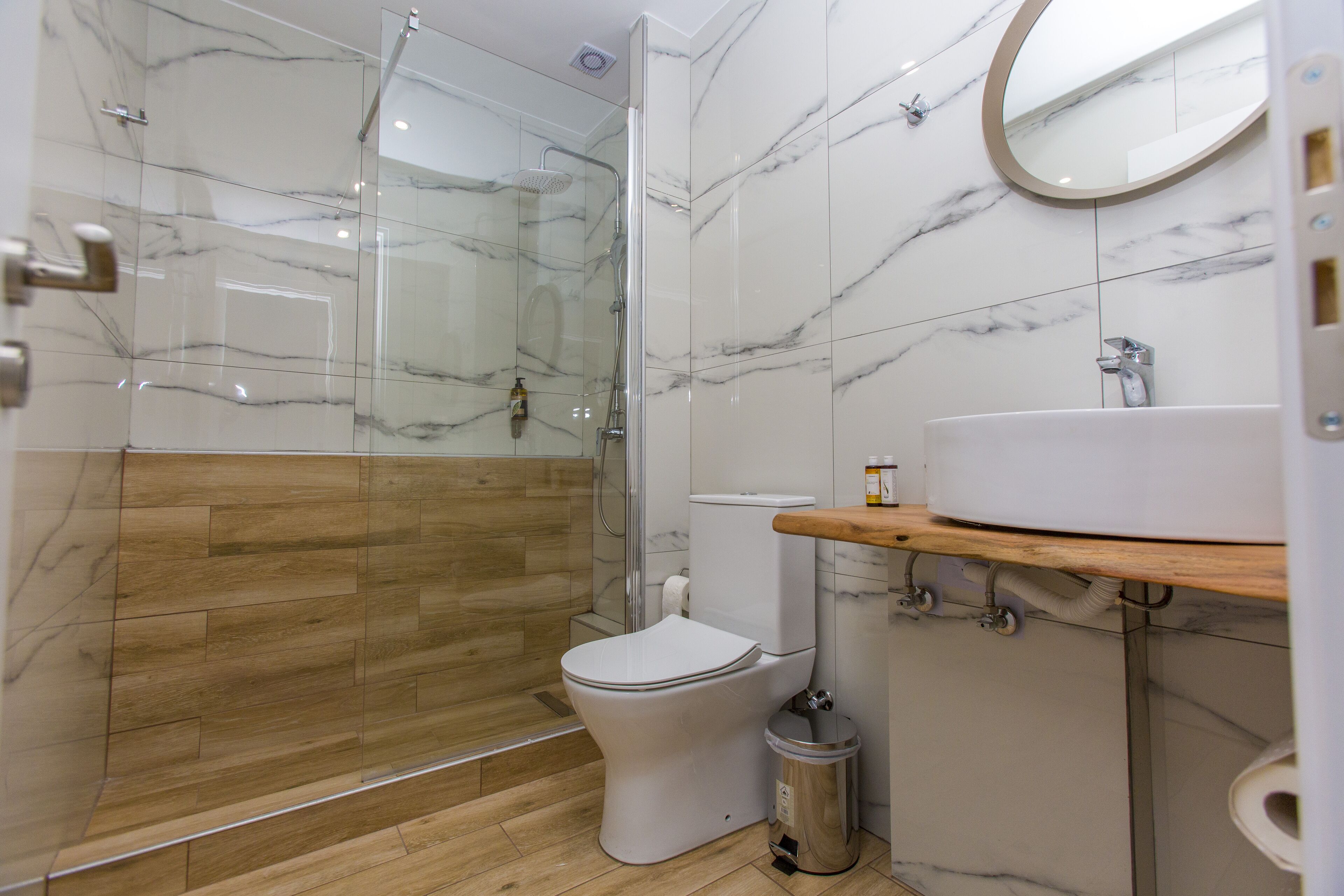 A modern bathroom with a glass-enclosed shower, a toilet, and a sink with a wooden countertop.