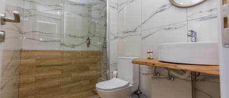 A modern bathroom with a glass-enclosed shower, a toilet, and a sink with a wooden countertop.