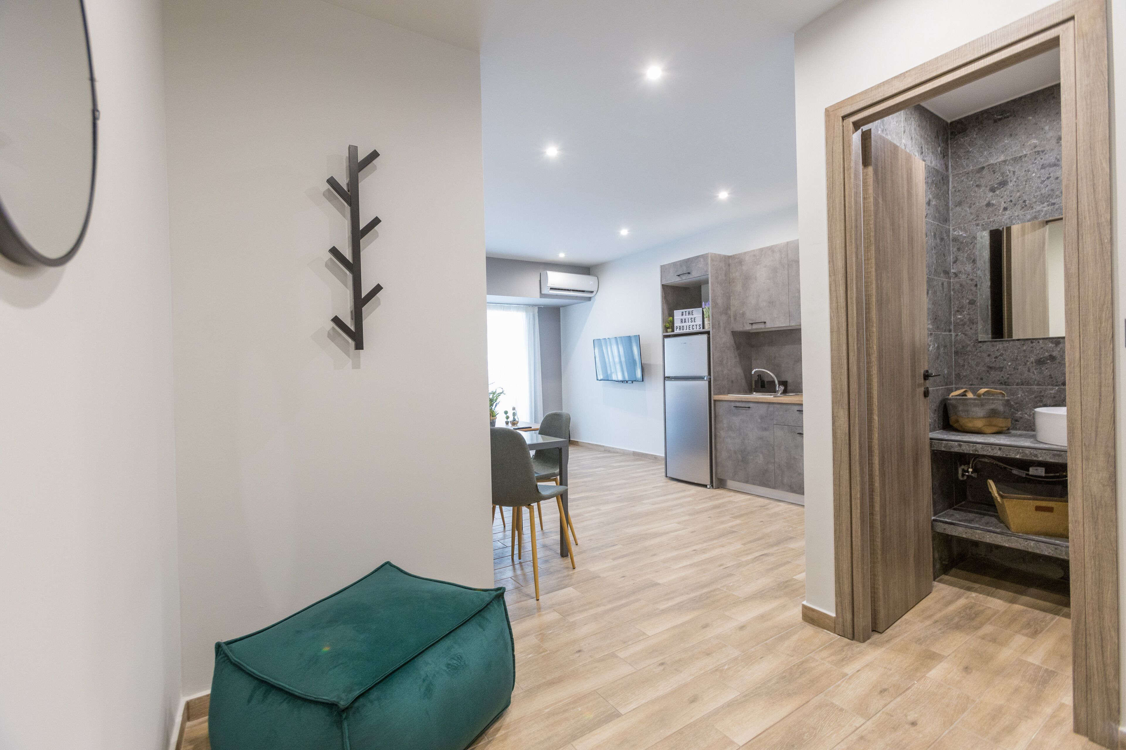 A modern kitchen with a built-in oven, a dining area with a green chair, and a wooden cabinet with a mirror.